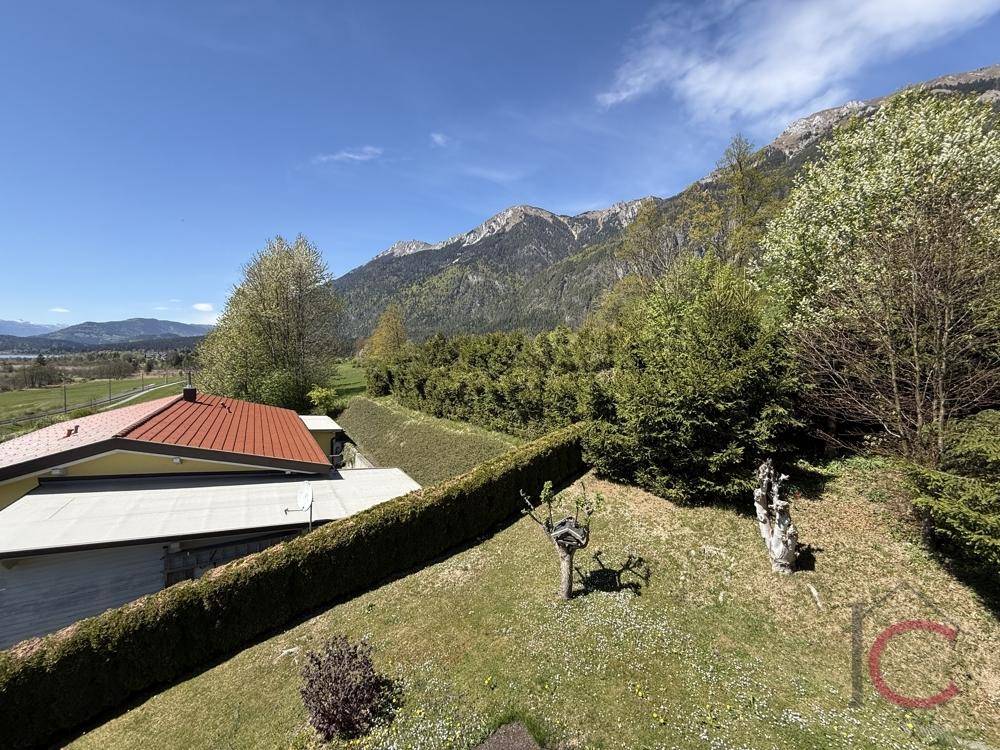 Weitläufiger Garten mit Hecke, Bäumen und Panoramablick auf die Berglandschaft.