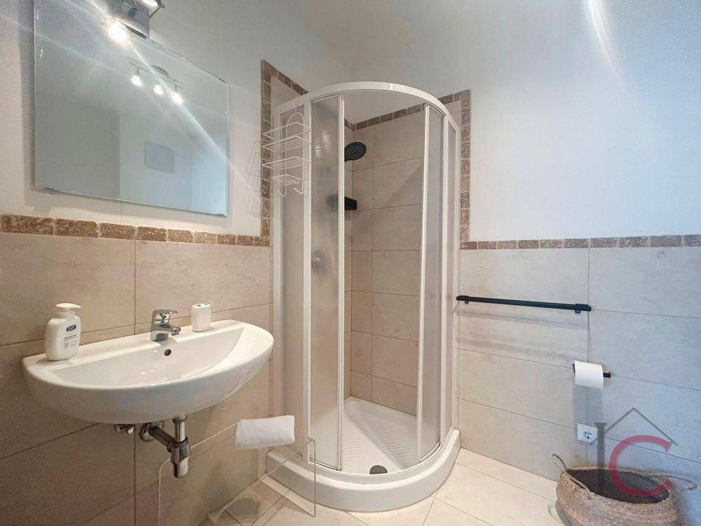 Modernes Badezimmer mit Duschkabine, Waschbecken und hellen Fliesen an Wänden und Boden.