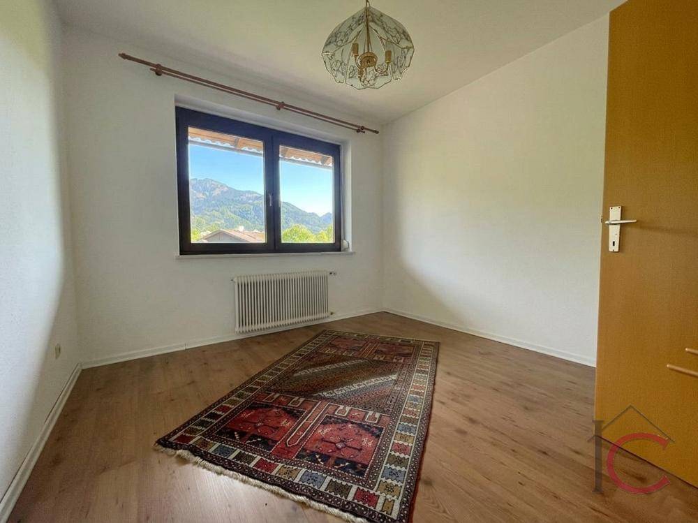 Helles Zimmer mit Holzboden und Fenster, das einen weiten Blick auf die Berge bietet.