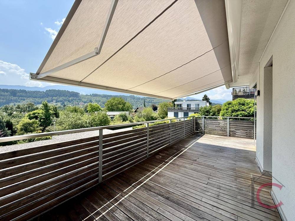 Helle Terrasse mit Holzbelag und ausgefahrener Sonnenmarkise, ideal für entspannte Stunden im Freien.