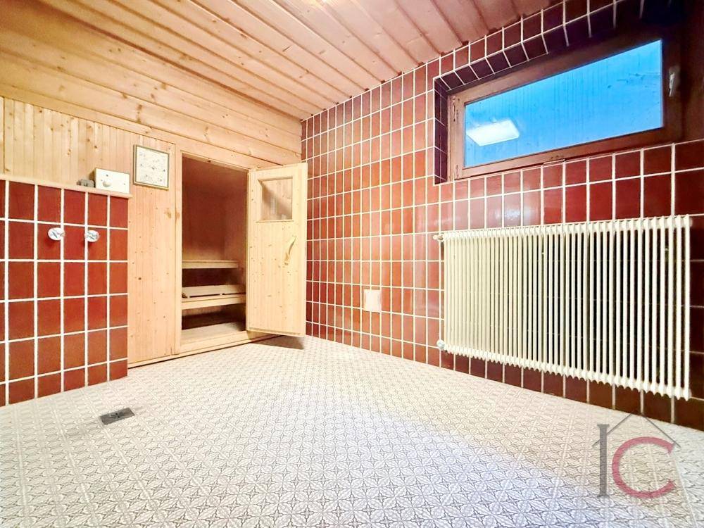 Saunabereich mit Holzverkleidung, Fenster und Heizkörper, ergänzt durch rote Wandfliesen.