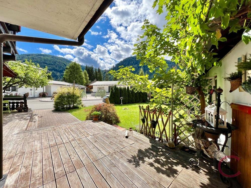 Holzterrasse mit Blick auf die umliegende Berglandschaft und viel Grün.