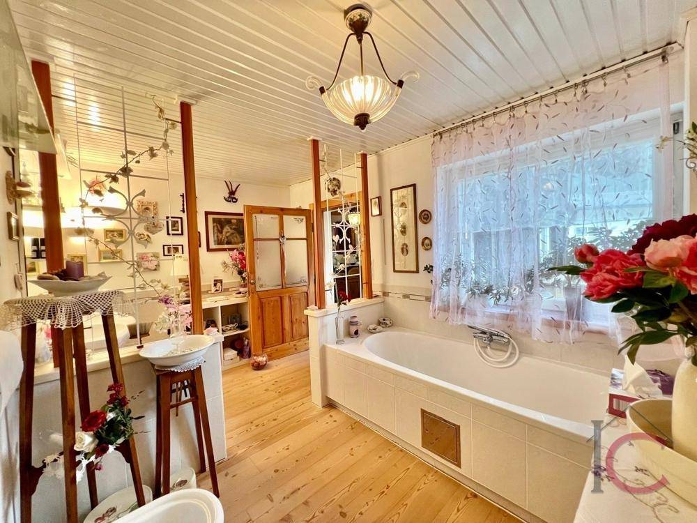 Geräumiges Badezimmer mit Badewanne, Holzboden und Fenster.
