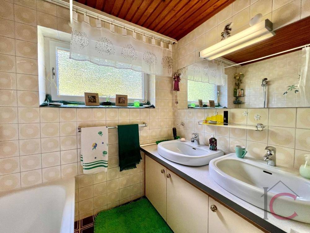 Badezimmer mit Doppelwaschbecken, Fenster und hellen Fliesen, funktional ausgestattet.