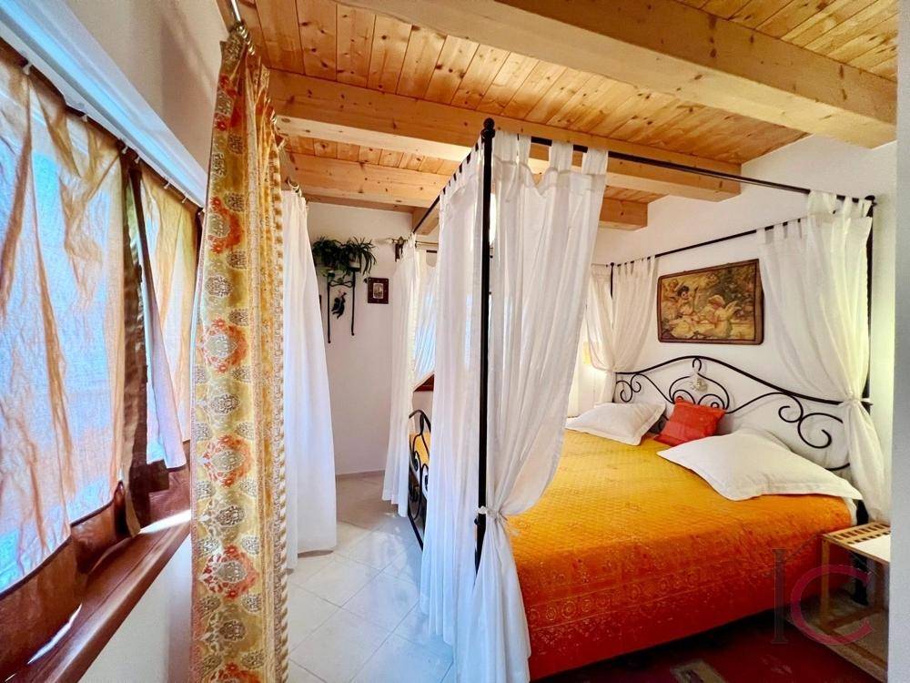 Romantisches Schlafzimmer mit Himmelbett, Holzbalkendecke und Fliesenboden.