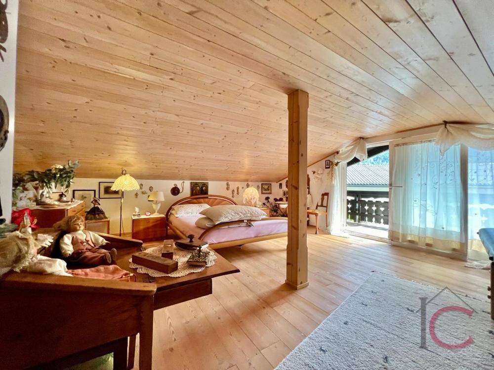Schlafzimmer im Dachgeschoss mit Holzboden, Holzbalkendecke und Zugang zum Balkon.