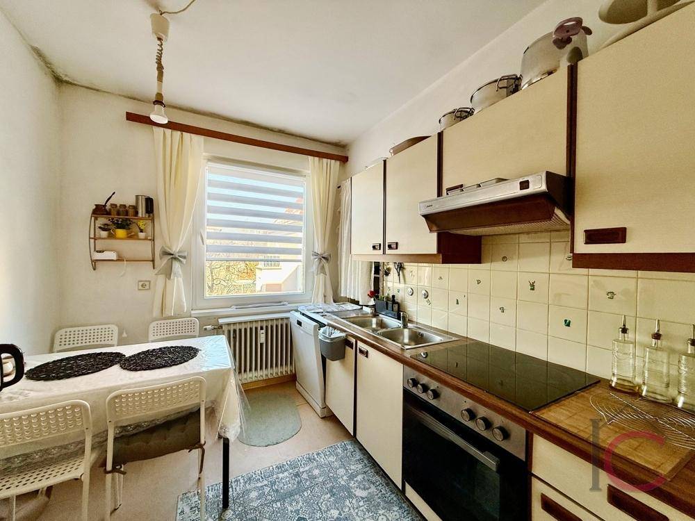 Funktionale Küche mit älteren Einbauschränken, Spüle und Essbereich am Fenster.