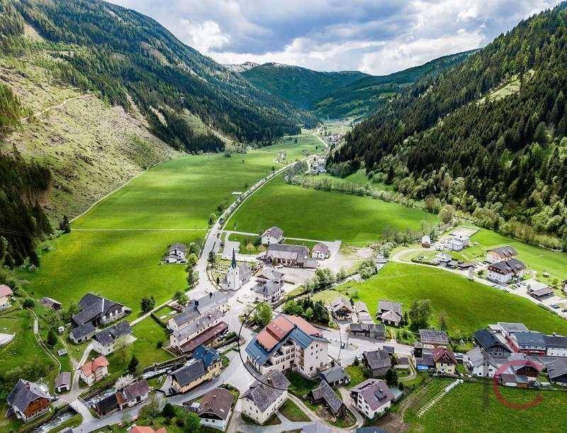 Luftaufnahme eines malerischen Dorfes in einem grünen Tal, umgeben von Bergen.
