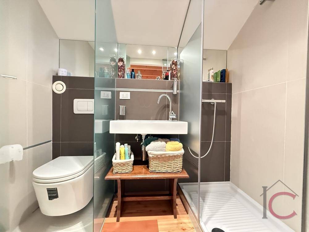 Modernes Badezimmer mit Dusche, wandhängendem WC und Waschtisch, durch Glas abgetrennt.
