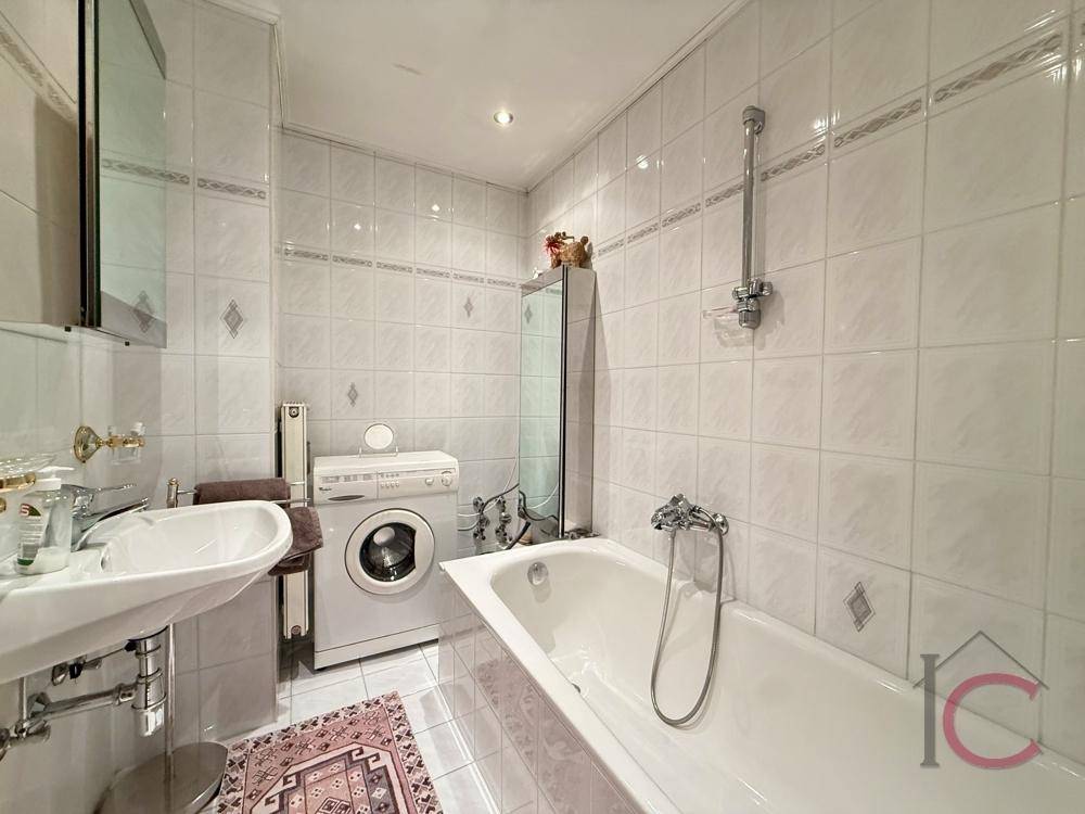 Funktionales Badezimmer mit Badewanne, Waschbecken und Waschmaschine, komplett gefliest.
