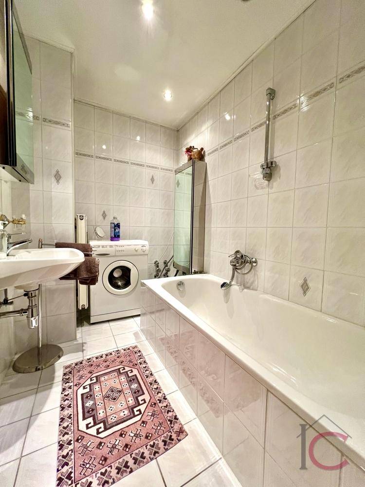 Helles Badezimmer mit Badewanne, Waschbecken und Waschmaschine, in gutem Zustand.