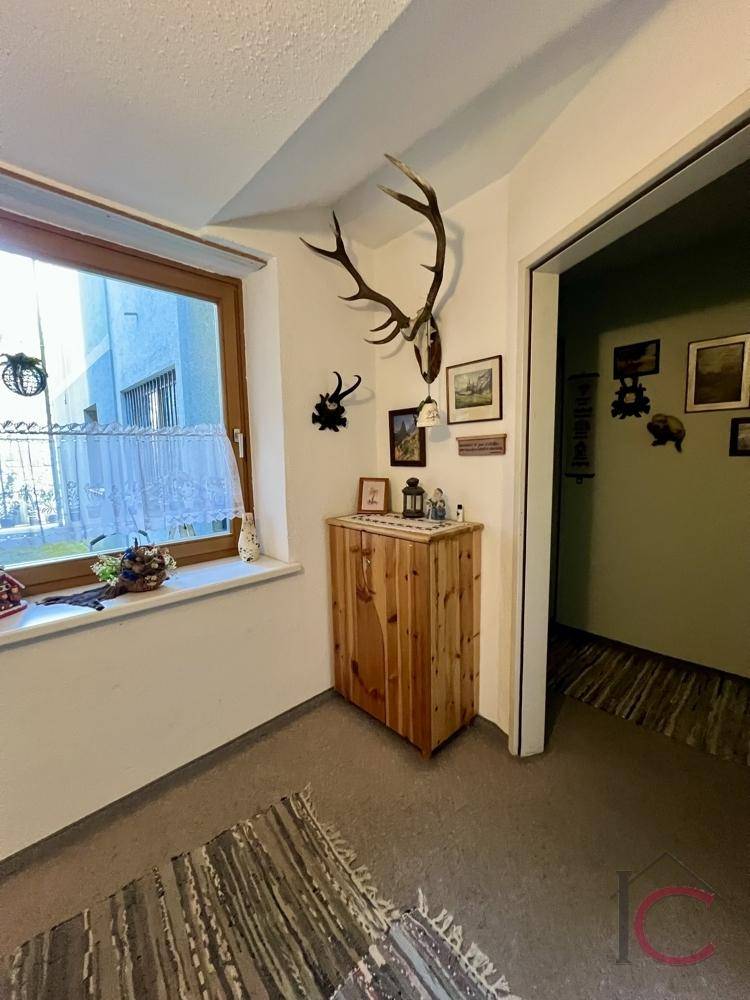 Gemütliche Ecke mit Fenster, kleinem Holzschrank und traditioneller Hirschgeweih-Dekoration.