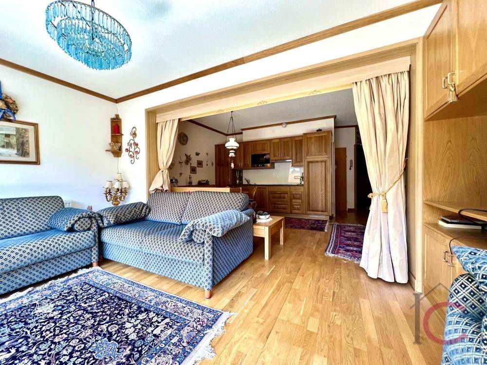 Gemütliches Wohnzimmer mit bequemen Sitzgelegenheiten und Blick auf die angrenzende, traditionelle Küche.