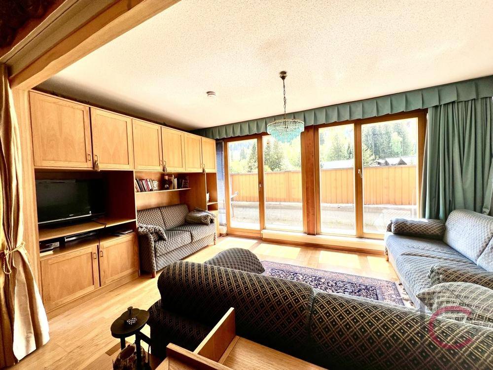 Lichtdurchflutetes Wohnzimmer mit Einbauschränken, bequemen Sofas und großen Fenstern mit grüner Aussicht.