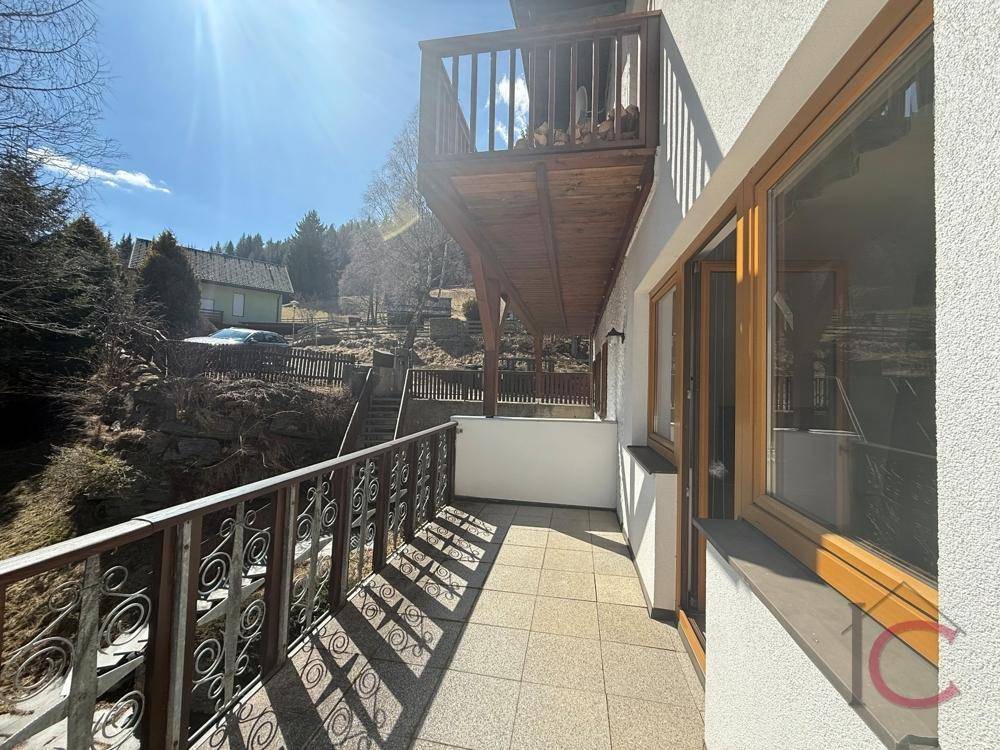 Langer Balkon mit Fliesenboden und schmiedeeisernem Geländer, sonnig und mit Blick ins Grüne.