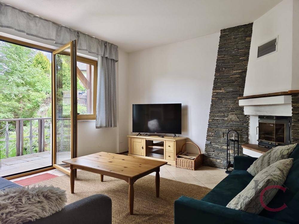 Wohnzimmer mit Kamin, Fernseher und geöffneter Balkontür, die viel Licht hereinlässt.