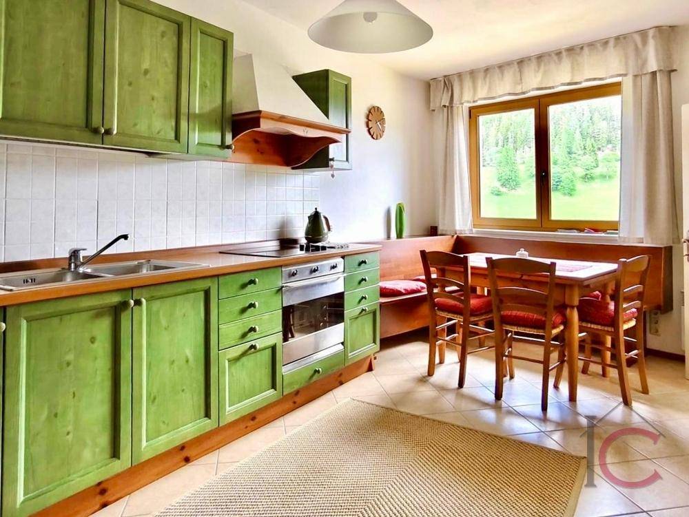Traditionelle Küche mit grünen Holzschränken, Essbereich und Fenster mit Blick ins Grüne.
