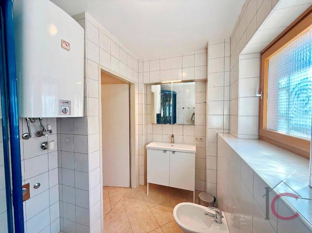 Badezimmer mit weißen Fliesen, Waschbecken, Bidet und Fenster für natürliches Licht.