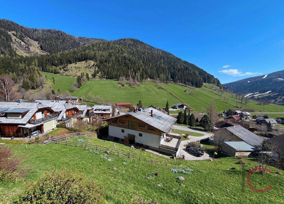 Weitläufiger Blick auf ein Dorf in einem grünen Tal, umgeben von bewaldeten Bergen.