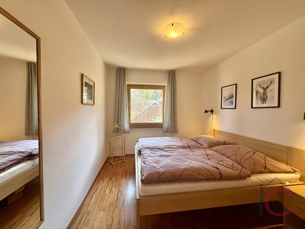 Schlafzimmer mit Doppelbett, Holzboden und großem Spiegel, hell und einladend.