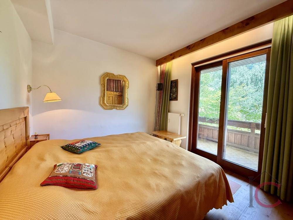 Schlafzimmer mit Holzbett, Parkettboden und großem Fenster mit Balkonzugang.