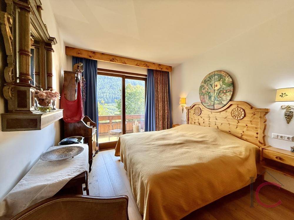 Schlafzimmer im alpinen Stil mit Holzbett, Parkettboden und Balkonzugang mit Bergblick.