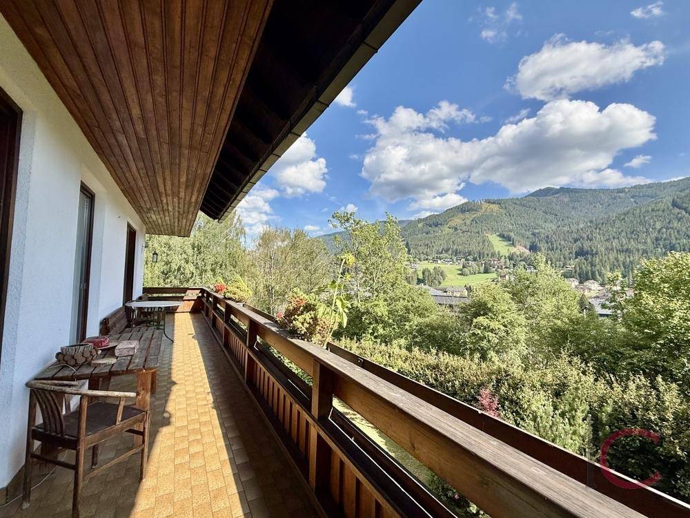 Langer Balkon mit Holzboden und Sitzgelegenheiten, bietet weitreichenden Blick auf die Berge.