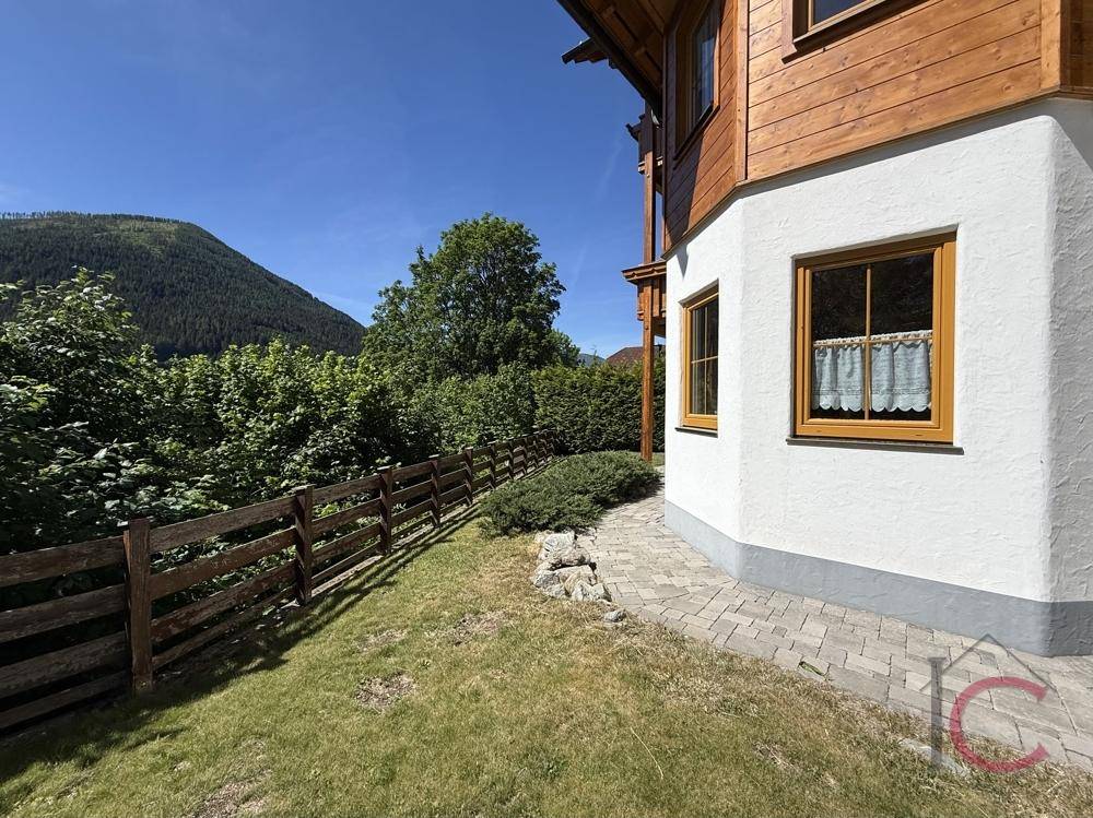 Seitenansicht des Hauses mit weißer Fassade, Holzelementen und einem grünen Gartenstreifen.