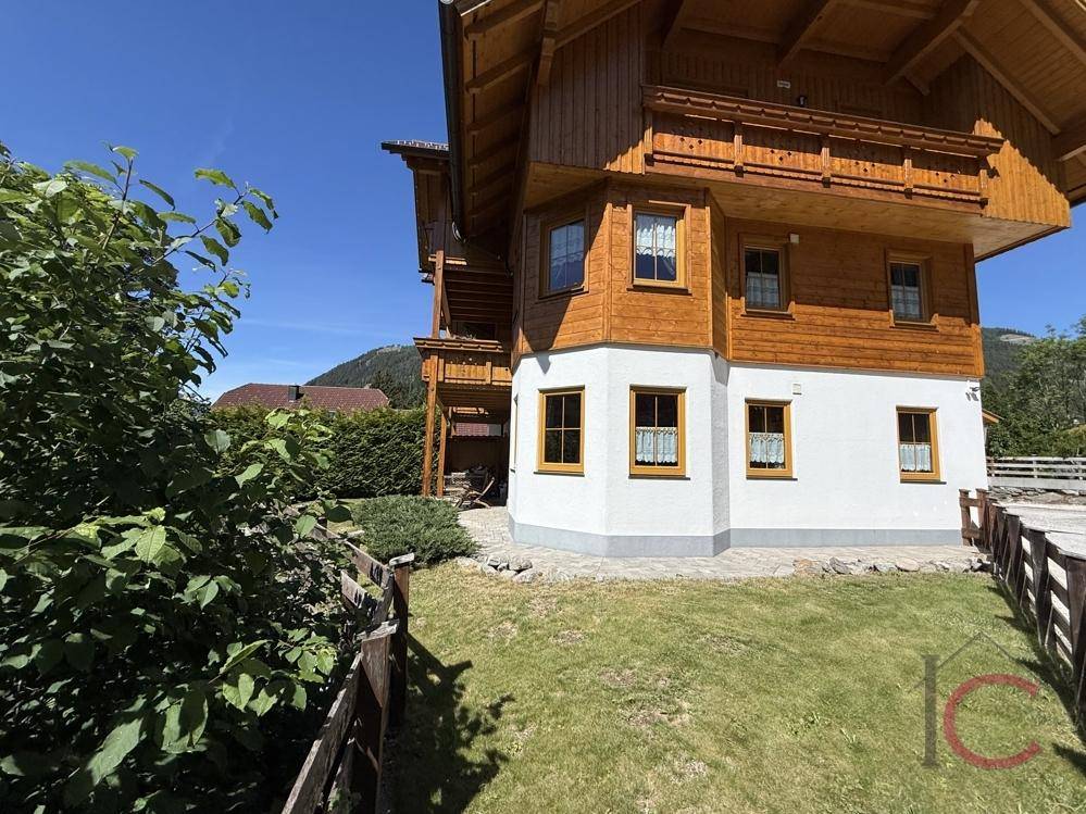 Traditionelles Holzhaus mit weißer Fassade und gepflegtem Gartenbereich in alpiner Umgebung.