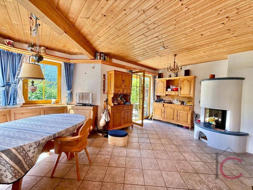 Geräumiger Wohn- und Essbereich mit Kachelofen, Holzbalken und Zugang zum Außenbereich.