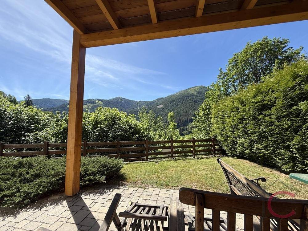 Überdachte Terrasse mit Gartenmöbeln und weitem Blick auf die bewaldeten Berge.