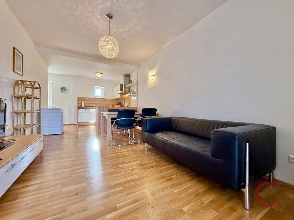 Heller Wohn- und Essbereich mit schwarzem Sofa und Holzboden, offen zur Küche.
