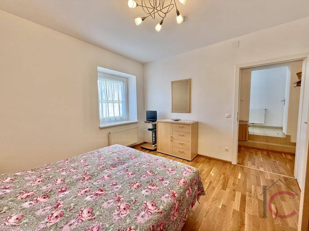Schlafzimmer mit Doppelbett und Holzboden, bietet Zugang zu einem angrenzenden Raum.