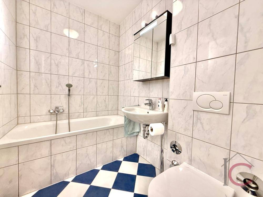 Modernes Badezimmer mit Badewanne, Waschbecken und auffälligem blau-weiß kariertem Fliesenboden.