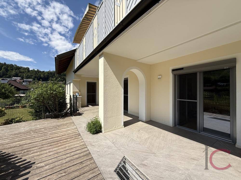 Geräumige, überdachte Loggia mit Fliesenboden und angrenzendem Holzdeck, bietet viel Platz im Freien.