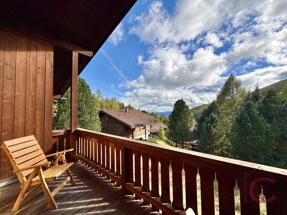 Langer Holzbalkon mit traditionellem Geländer und malerischem Blick auf die Alpen.