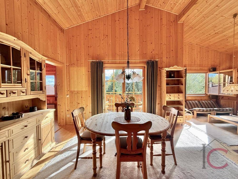 Warmer Essbereich mit Holztisch, passenden Stühlen und Blick durch große Fenster.