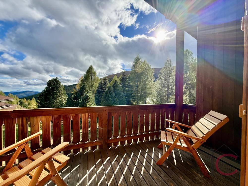Geräumiger Holzbalkon mit bequemen Stühlen und Panoramablick auf die umliegenden Berge.