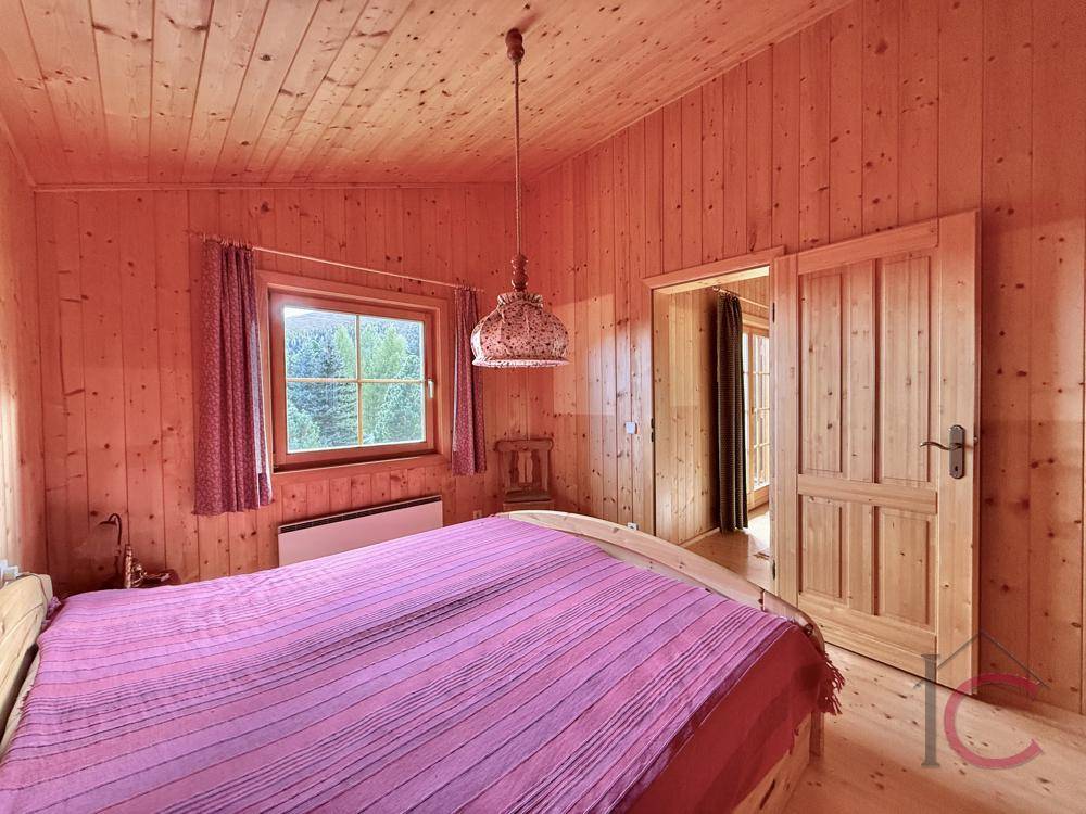 Gemütliches Schlafzimmer mit Holzvertäfelung, Doppelbett und Fenster mit Bergblick.
