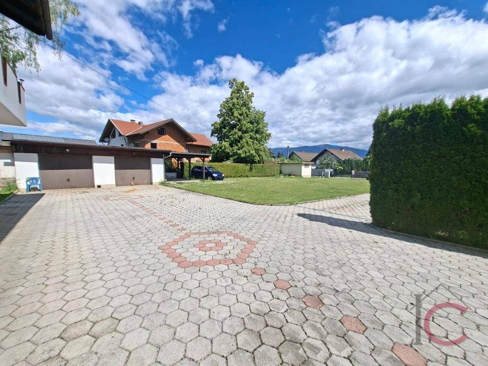 Gepflasterter Vorplatz mit Garage und Carport, umgeben von Grünflächen und Hecken.