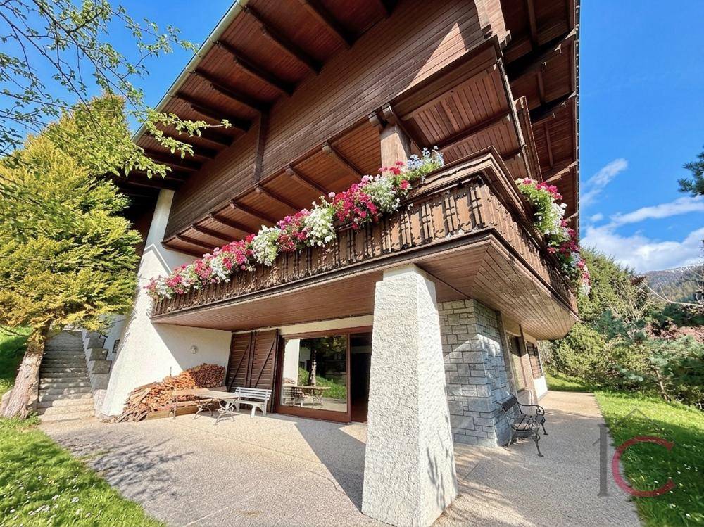 Traditionelles Holzhaus mit Balkonen, Steinsockel und kleiner Terrasse im Grünen.