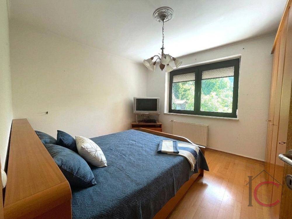 Schlafzimmer mit Doppelbett, hellem Laminatboden und Fenster mit Blick ins Grüne.