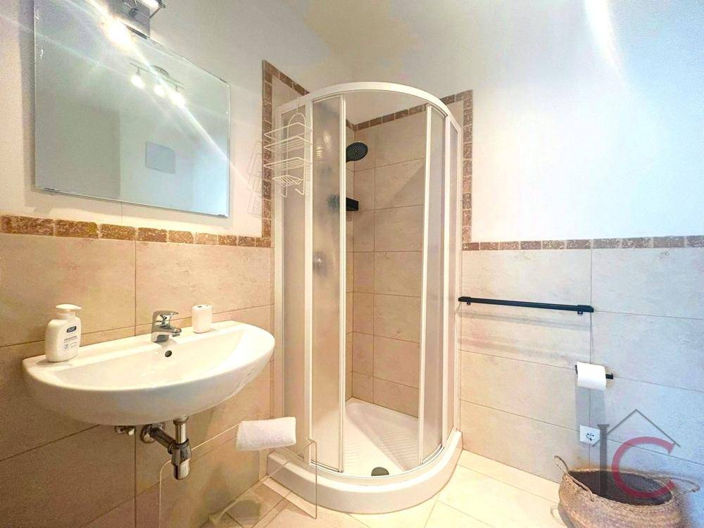 Funktionales Badezimmer mit Waschbecken, Spiegel und einer praktischen Eckduschkabine.