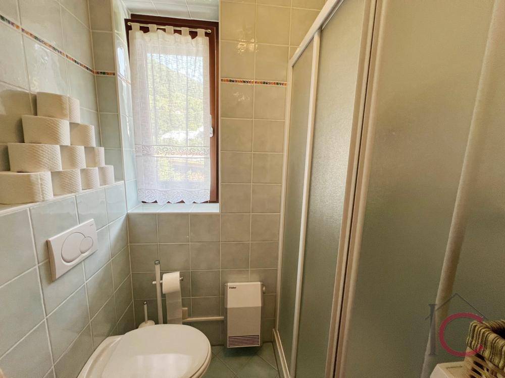Kleines Badezimmer mit hellgrünen Fliesen, Toilette, Duschkabine und Fenster für Tageslicht.