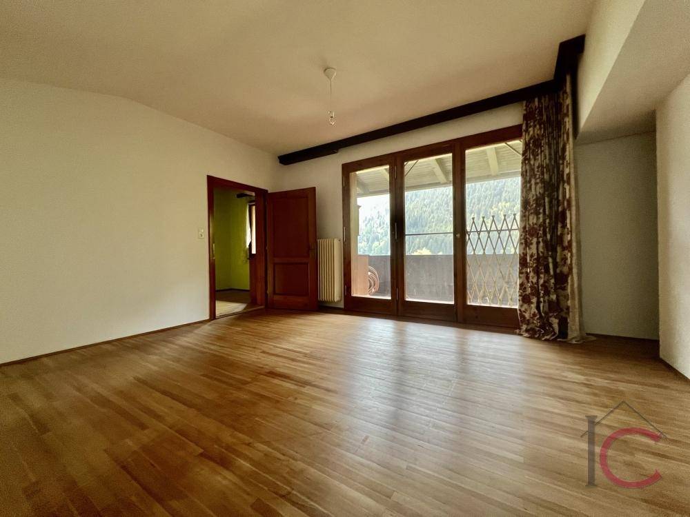 Geräumiger Raum mit Holzboden und großem Balkonzugang, bietet viel Tageslicht.