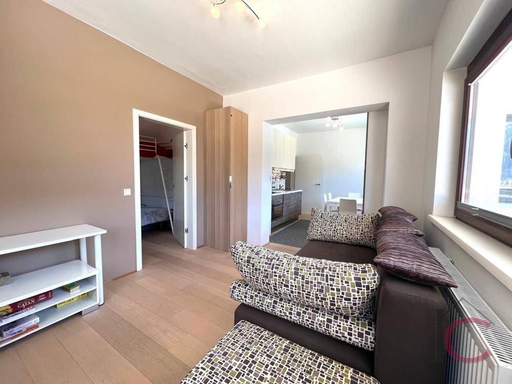 Helles Wohnzimmer mit Holzboden, Blick in die Küche und Zugang zu einem weiteren Zimmer.
