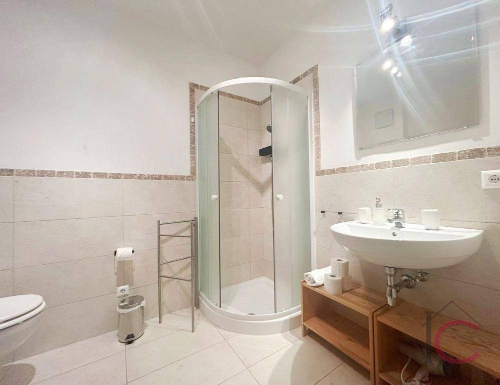 Funktionales Badezimmer mit Duschkabine, WC, Waschbecken und hellen Wand- und Bodenfliesen.