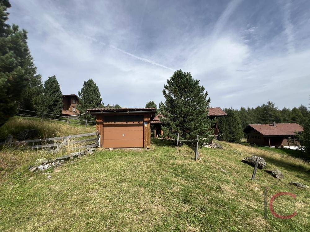 Kleines Holzgebäude mit Garagentor in ländlicher Umgebung, umgeben von grünen Wiesen.