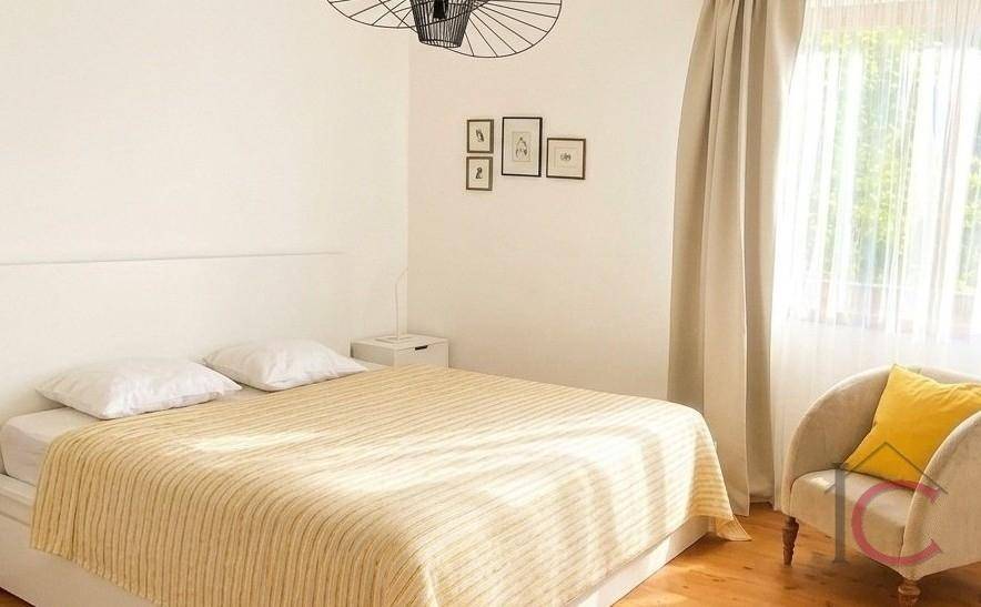 Helles Schlafzimmer mit Doppelbett, Holzboden und einem Fenster, das viel Tageslicht hereinlässt.