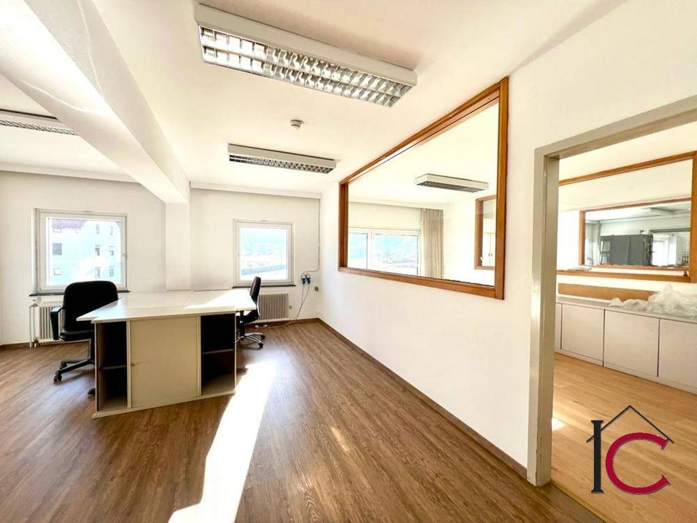 Helles Büro mit Laminatboden, großen Fenstern und einem großen Spiegel an der Wand.
